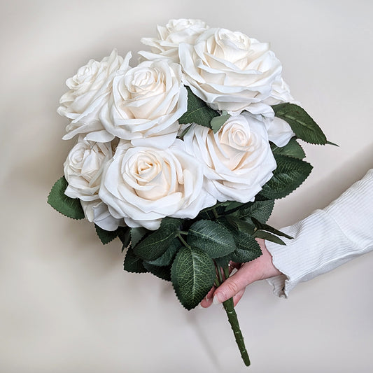 Hand präsentiert einen künstlichen Rosenstrauß mit weißen Blüten vor hellem Hintergrund