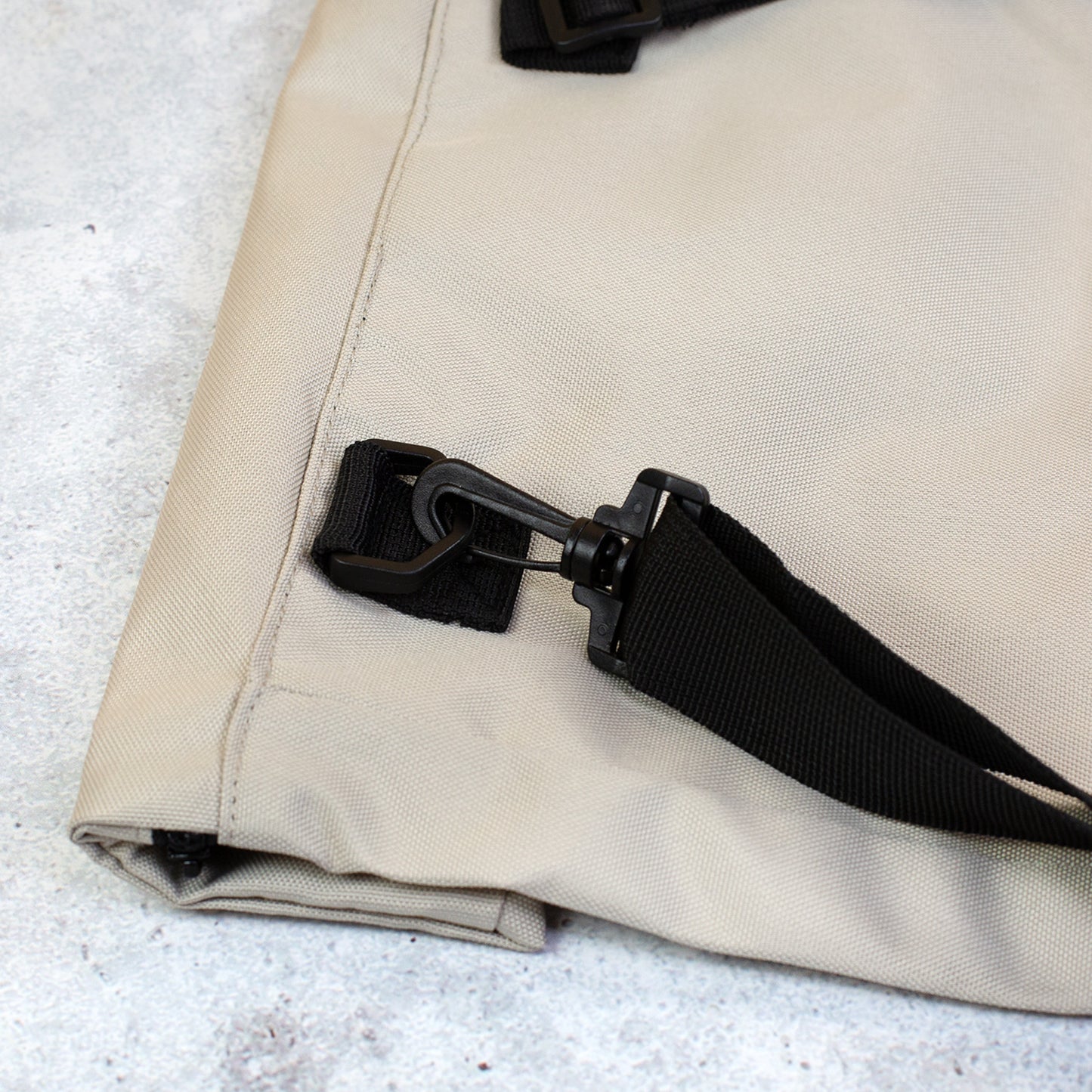 Nahaufnahme der Befestigung am beigen Rucksack mit schwarzem Schultergurt und Karabiner