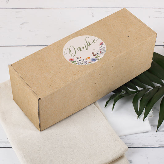 Geschenkverpackung mit naturbraunem Druck und aufgedrucktem Danke-Kreis, dekoriert mit Palmblatt und Stofftüchern