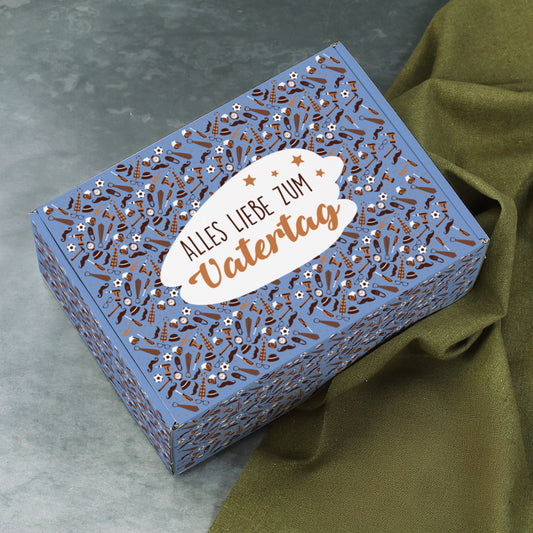 Geschenkverpackung zum Vatertag auf grauem Untergrund, seitlich geöffnet mit Olivstoff im Hintergrund.