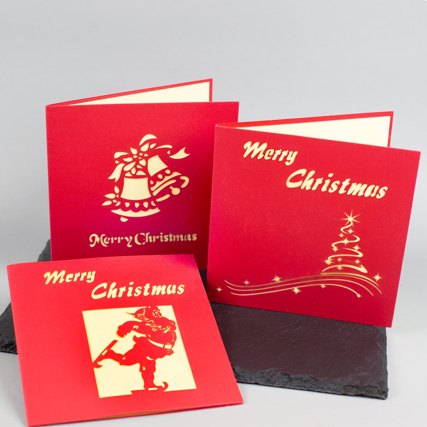Drei rote Weihnachtskarten mit goldgelbem Innenleben und „Merry Christmas“-Schriftzug in verschiedenen Designs – Weihnachtsmann, Glocken und Tannenbaum.