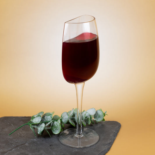 Scherz-Weinglas mit halbierter Optik und versetzter Glaskante, gefüllt mit Rotwein, moderne Präsentation vor warmem Hintergrund