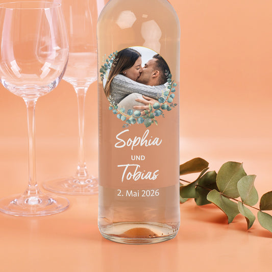 Personalisierte Weißweinflasche mit Foto im Eukalyptuskranz, Namen „Sophia und Tobias“ und Hochzeitsdatum.