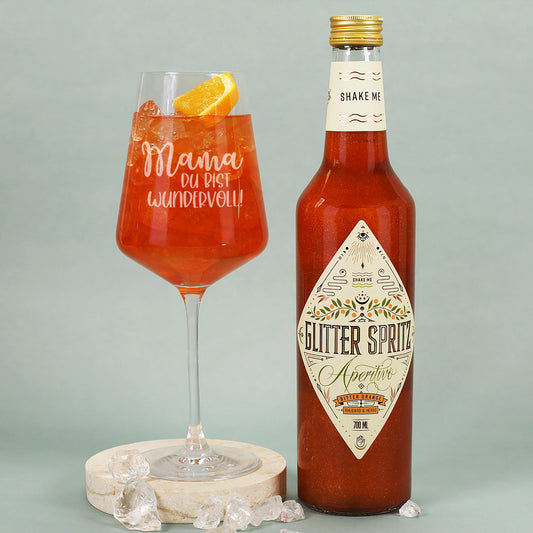 Glitter Spritz mit graviertem Cocktailglas „Mama, du bist wundervoll!“ auf heller Unterlage mit Eiswürfeln und Orangenscheibe