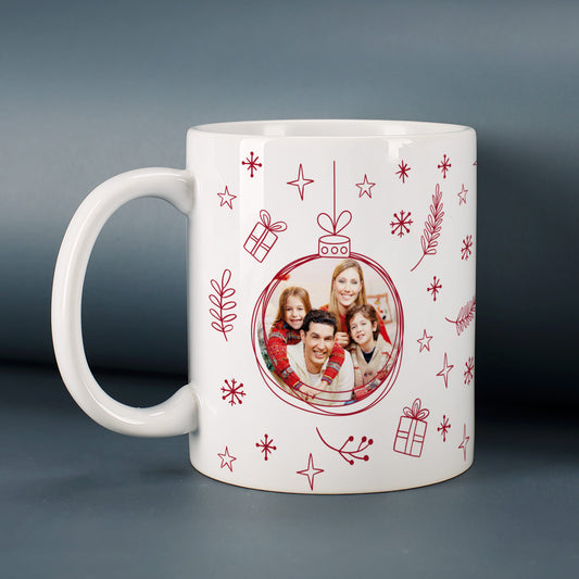 Personalisierbare Weihnachtstasse mit rotem Weihnachtskugel-Motiv und Familienfoto, auf grauem Hintergrund platziert.
