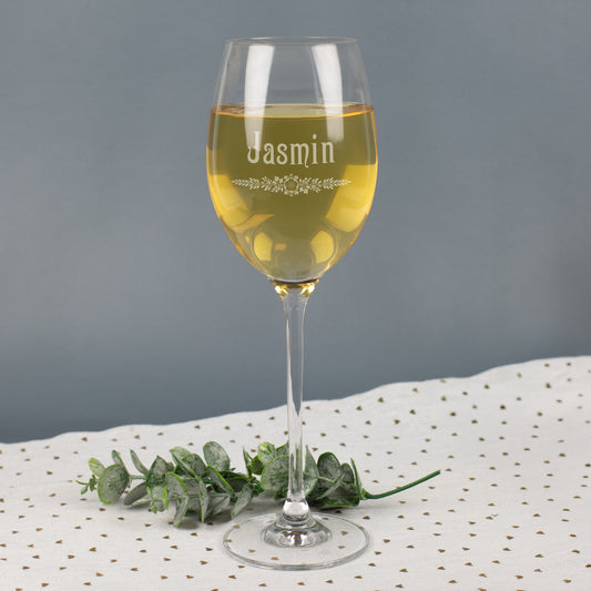 Leonardo Weißweinglas mit Gravur Jasmin und floralem Blätter-Ornament, gefüllt mit Weißwein, auf grauem Hintergrund