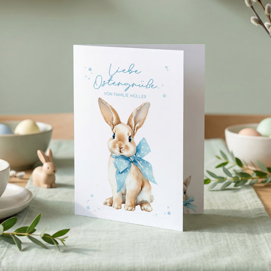 Personalisierte Osterkarte mit Schriftzug Liebe Ostergrüße und Osterhase mit Schleife auf weißem Karton