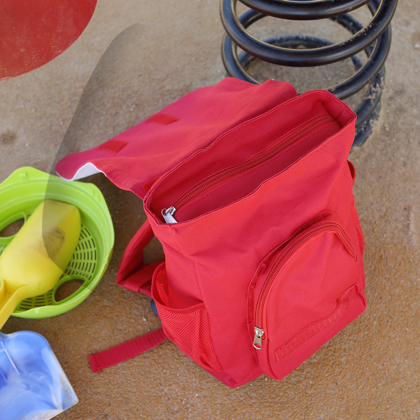 Geöffneter roter Kinder Rucksack mit Hauptfach, Reißverschlüssen und seitlichem Netzfach auf dem Spielplatz