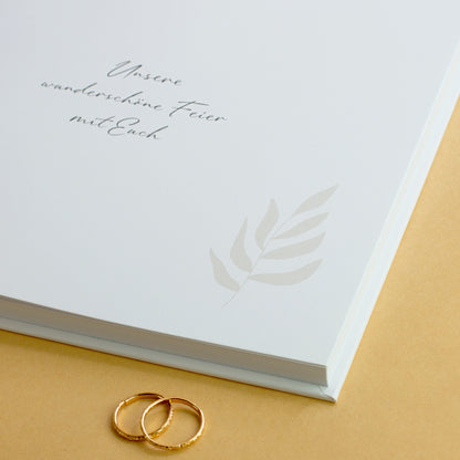 Innenseite Gästebuch Hochzeit mit zartem Schriftzug „Unsere wunderschöne Feier mit Euch“ und Eheringen