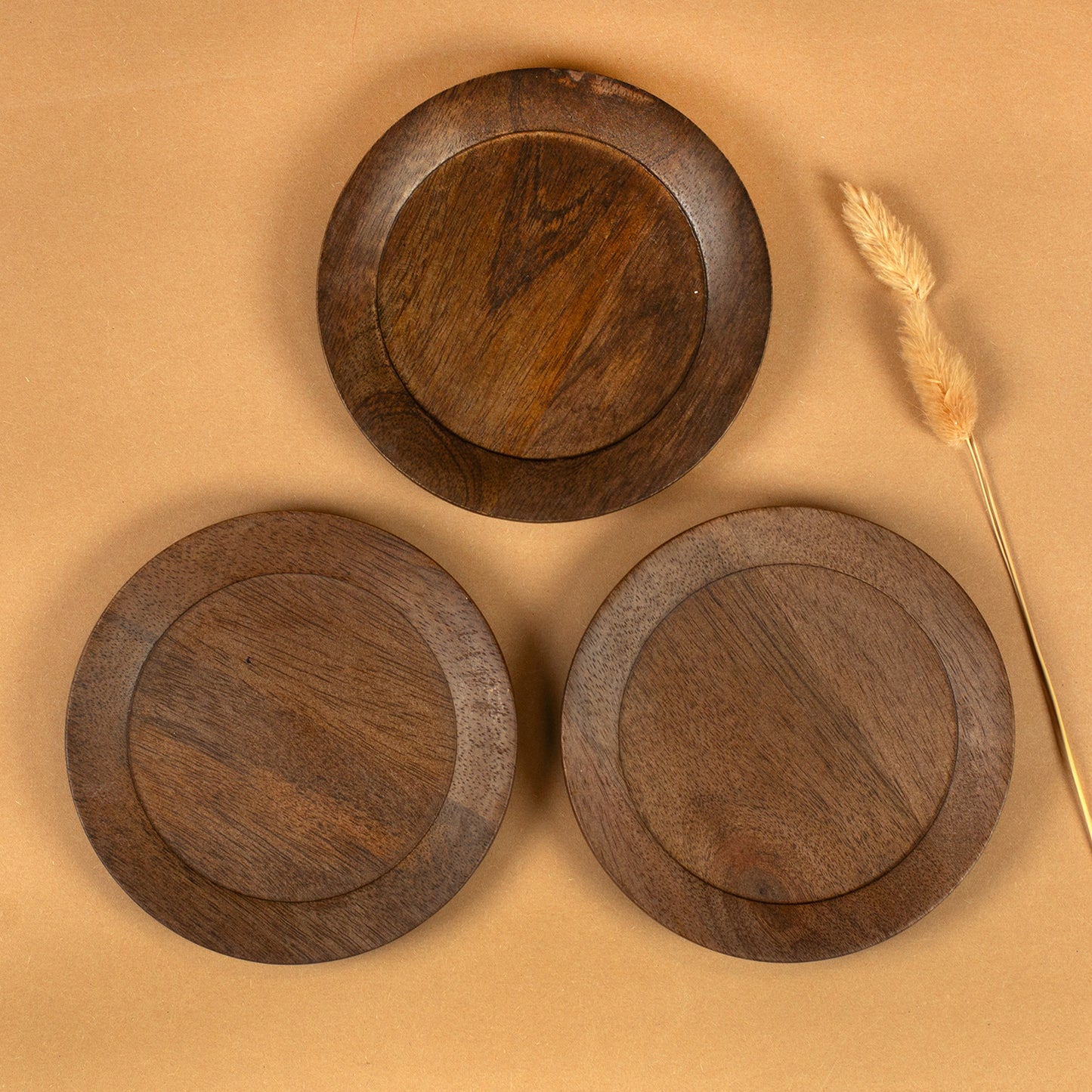 Drei runde Kerzenteller aus braunem Akazienholz von oben mit sichtbarer Holzmaserung und Trockenblume