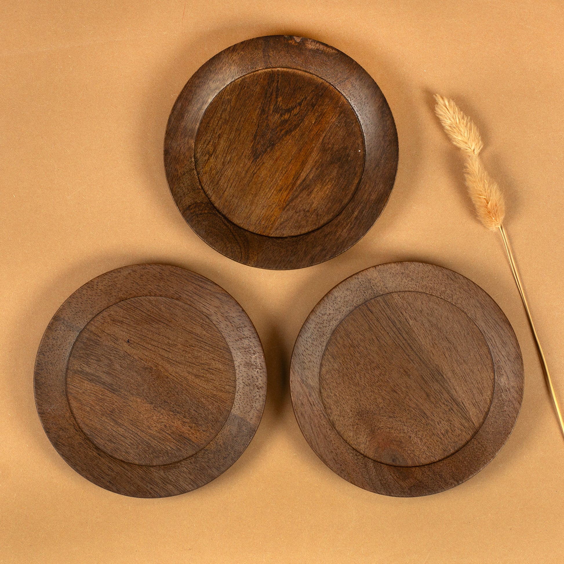 Drei runde Kerzenteller aus braunem Akazienholz von oben mit sichtbarer Holzmaserung und Trockenblume