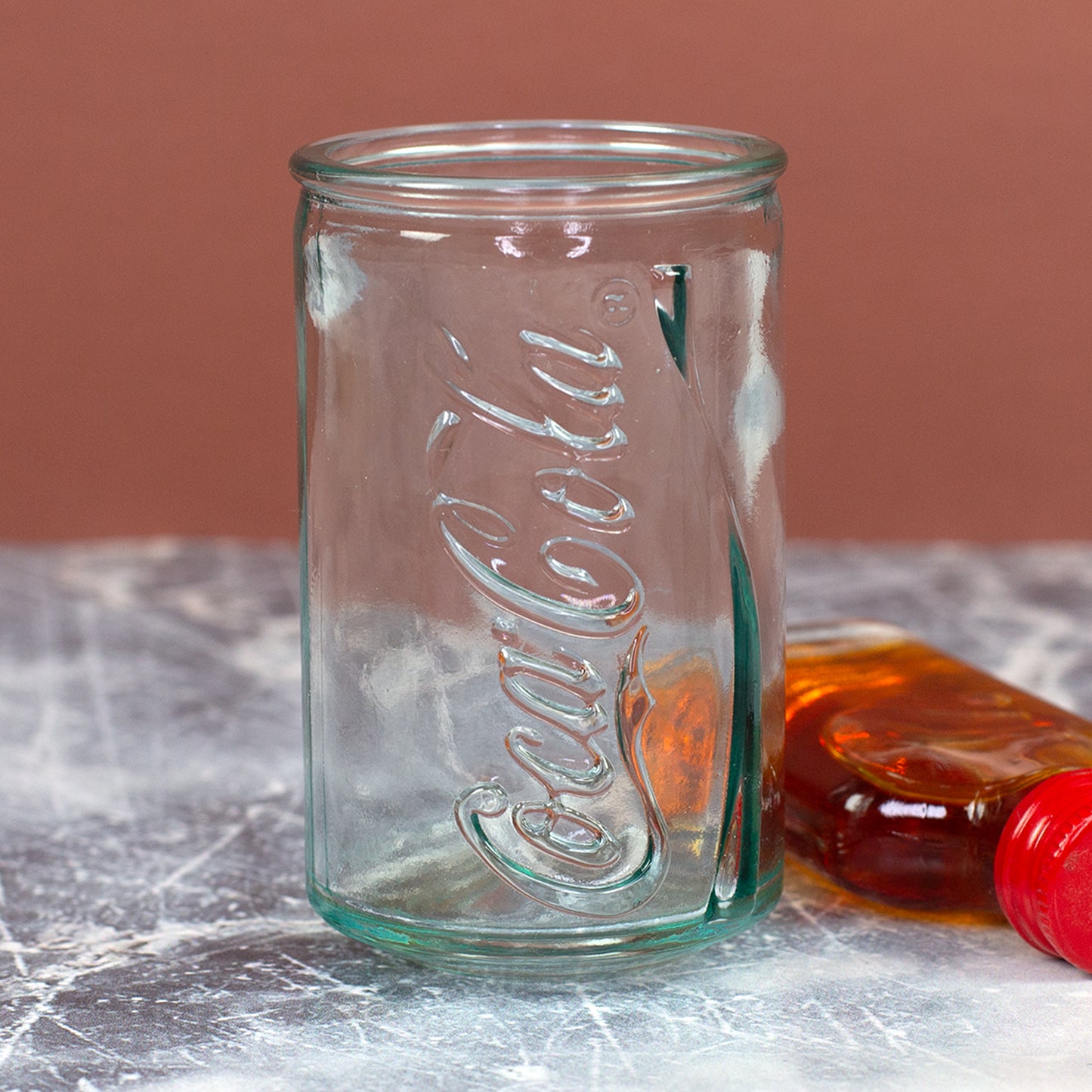 Aufrecht stehendes Coca-Cola Shotglas im Retro-Dosen-Look mit geprägtem Schriftzug und kleiner Flasche