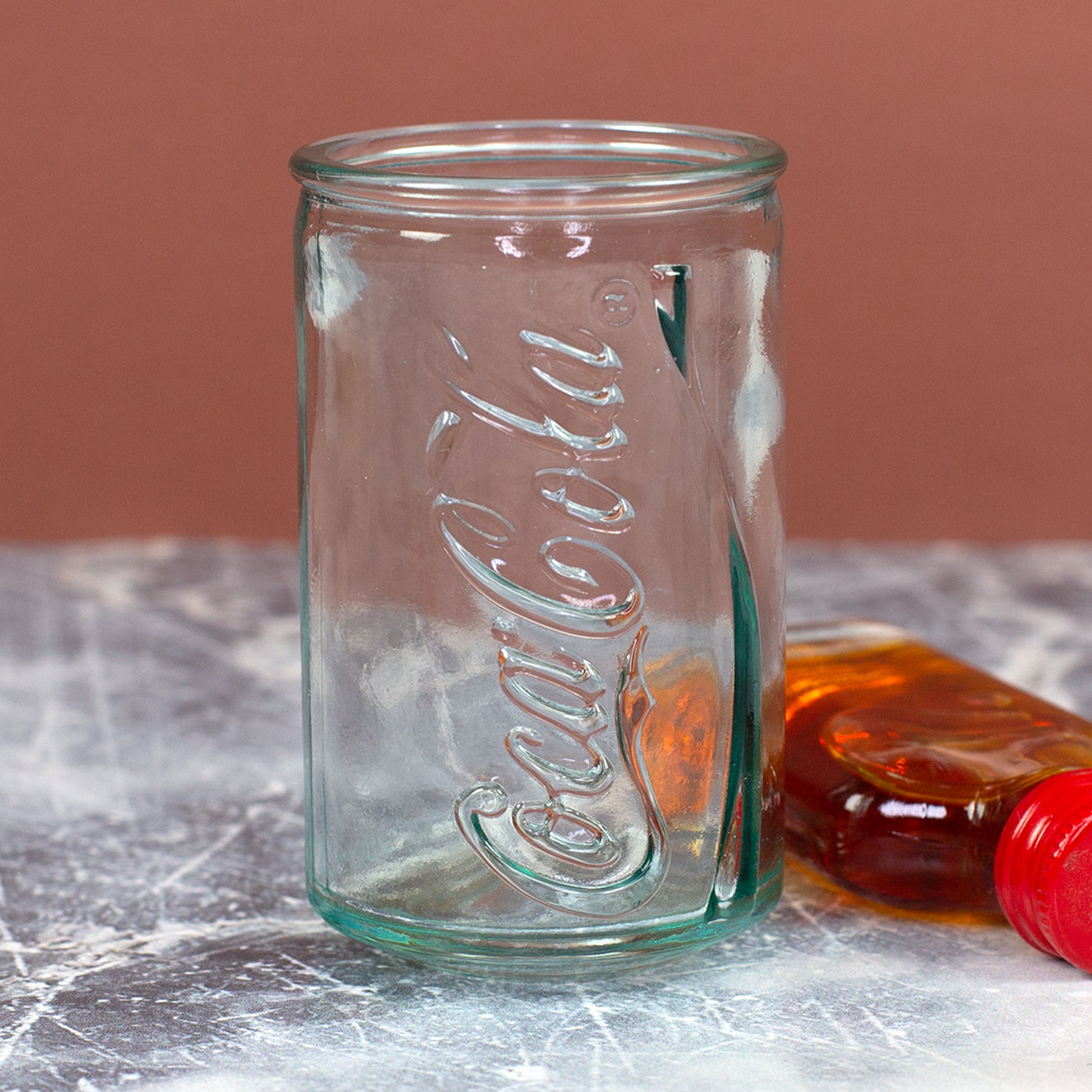 Aufrecht stehendes Coca-Cola Shotglas im Retro-Dosen-Look mit geprägtem Schriftzug und kleiner Flasche