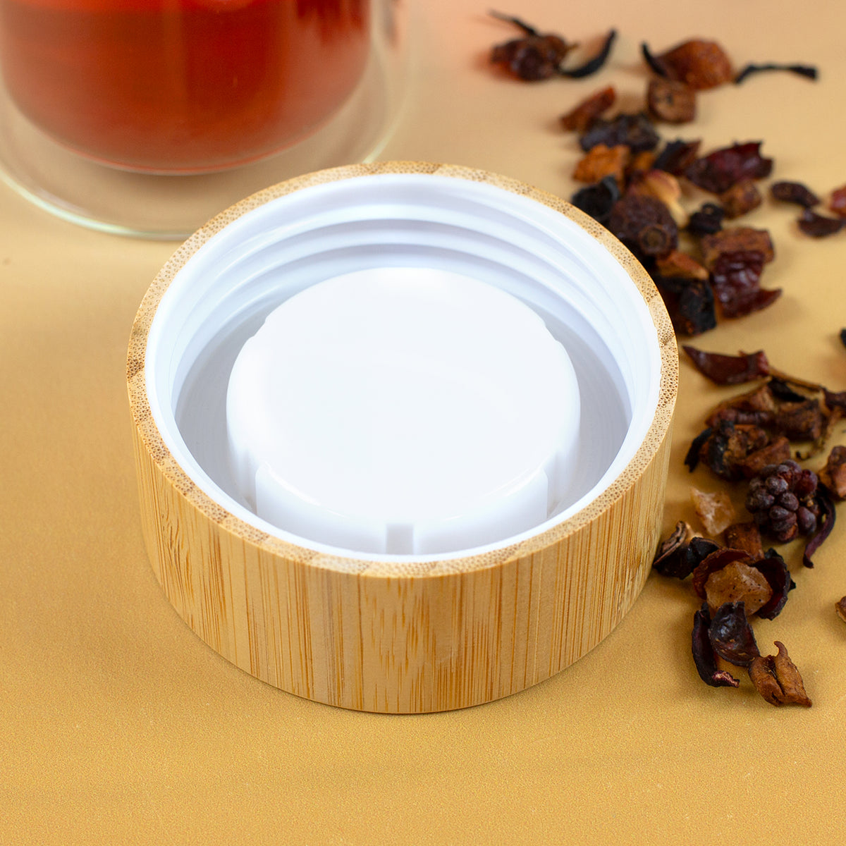 Innenseite des Bambusdeckels mit weißem Schraubverschluss neben losem Früchtetee und Glasflasche