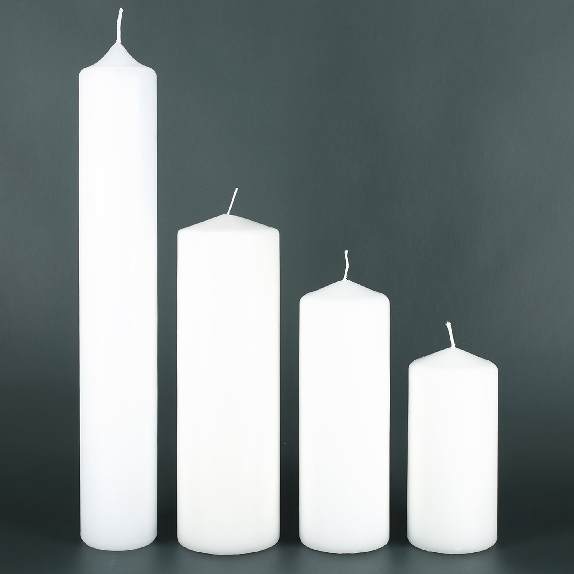 Größenvergleich Kerzen – vier weiße Stumpenkerzen in unterschiedlichen Höhen als Übersicht