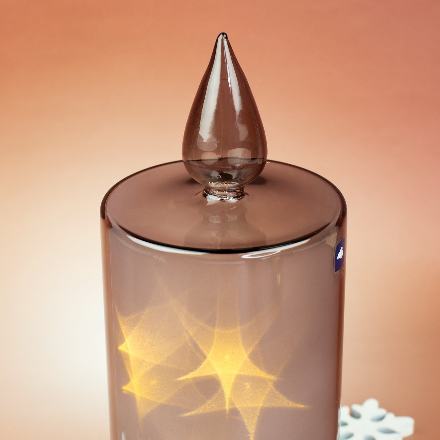 Detailaufnahme der Glasflamme der Leonardo LED-Kerze mit warmen Lichtreflexionen im grauen, lackierten Glaszylinder.