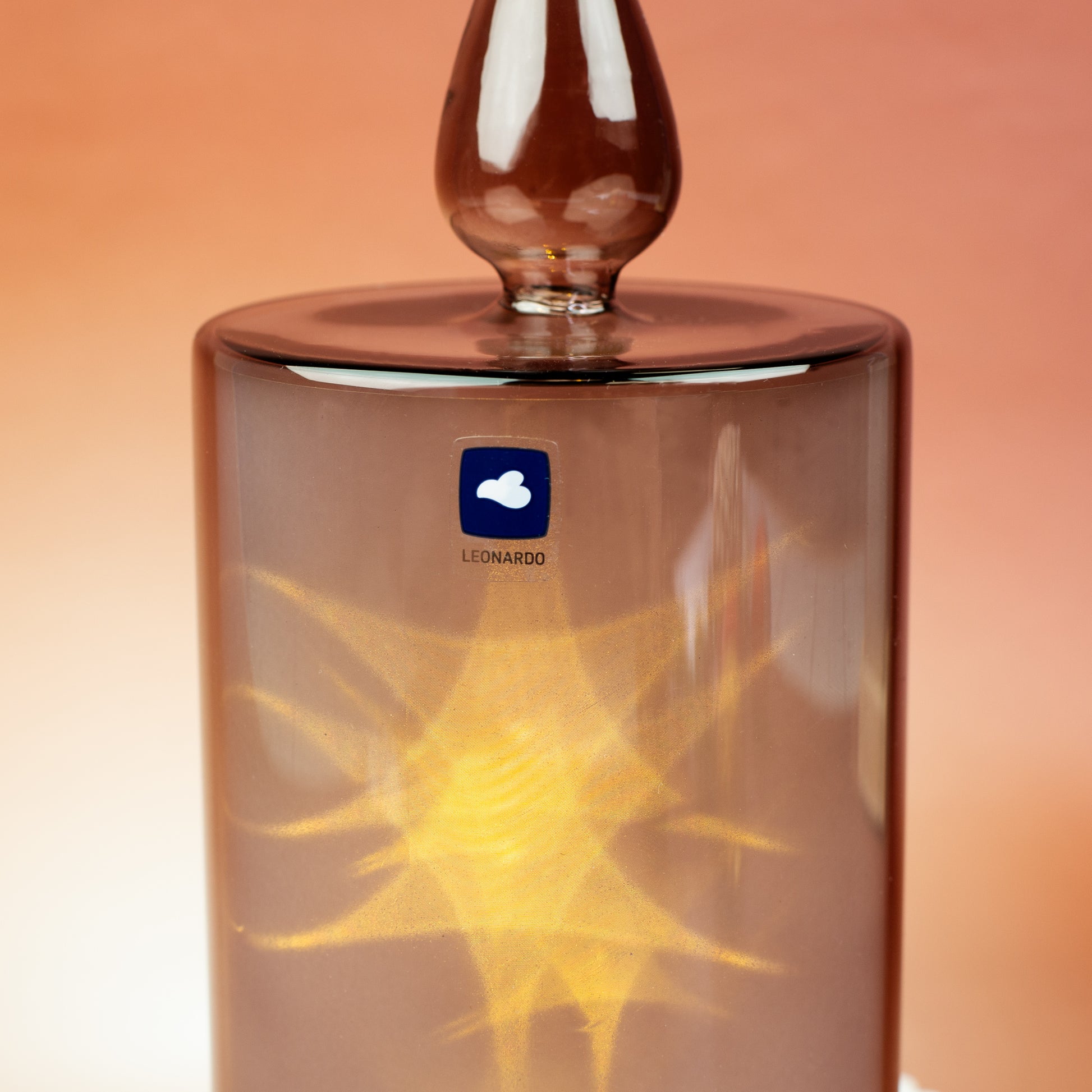 Seitliche Detailansicht der Leonardo LED-Kerze mit sichtbarem Herstellerlogo und warm leuchtendem LED-Licht im grauen Glas.