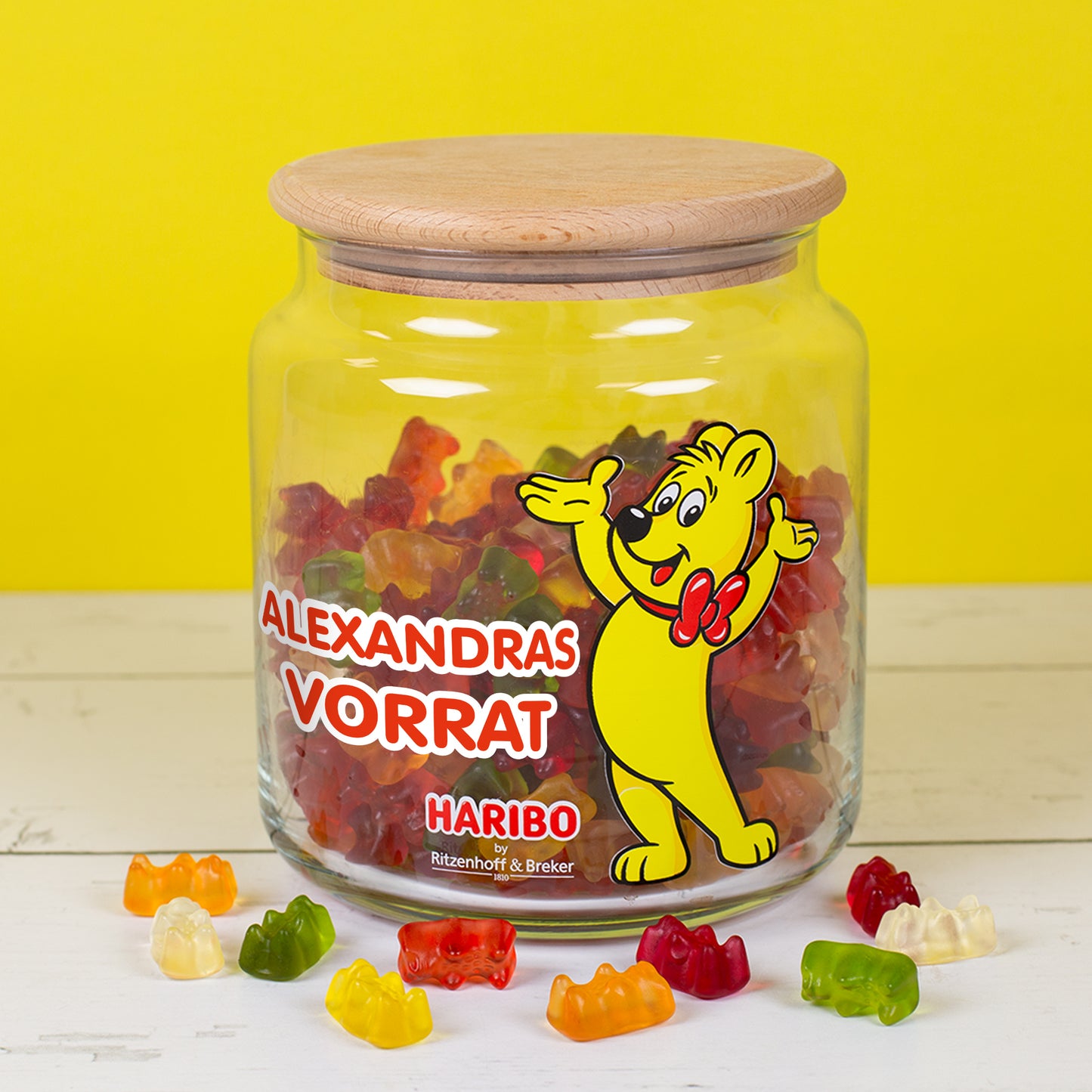 Personalisierte HARIBO Glasdose mit Aufdruck ‚Alexandras Vorrat‘ und Goldbär, gefüllt mit Gummibärchen, geschlossen mit Holzdeckel.
