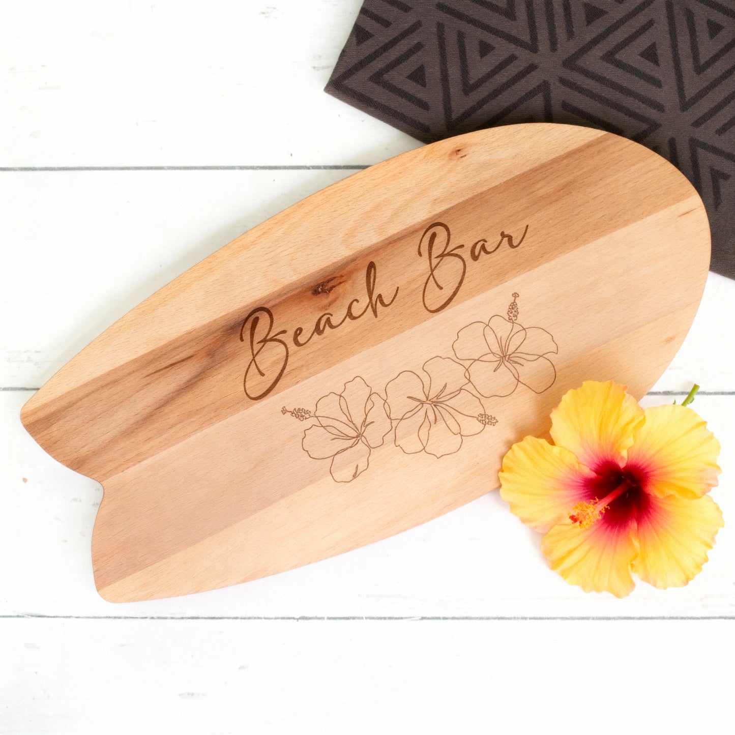 Surfbrett-Servierbrett aus Holz mit Hibiskusgravur und gelber Blüte als sommerliche Dekoration