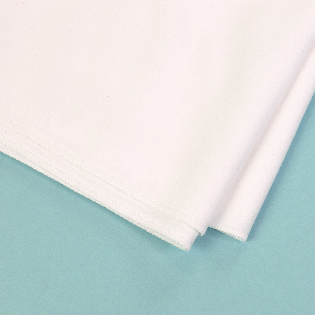 Detailaufnahme von Material und Naht eines weißen Sporthandtuchs auf türkisem Hintergrund