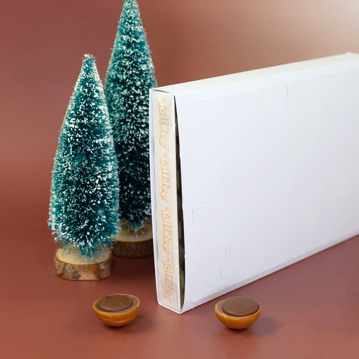 Seitenansicht des Toffifee Adventskalenders mit Weihnachtsdeko und Tannenbäumen