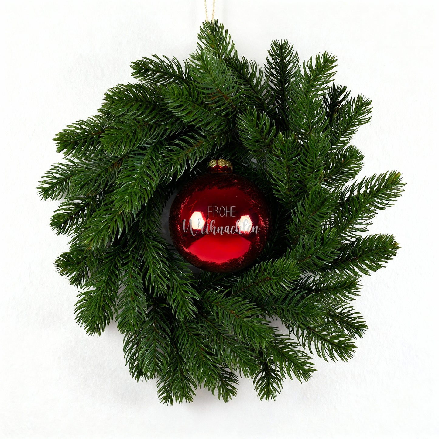 Weihnachtskranz mit roter gravierter Kugel Frohe Weihnachten auf weißem Untergrund