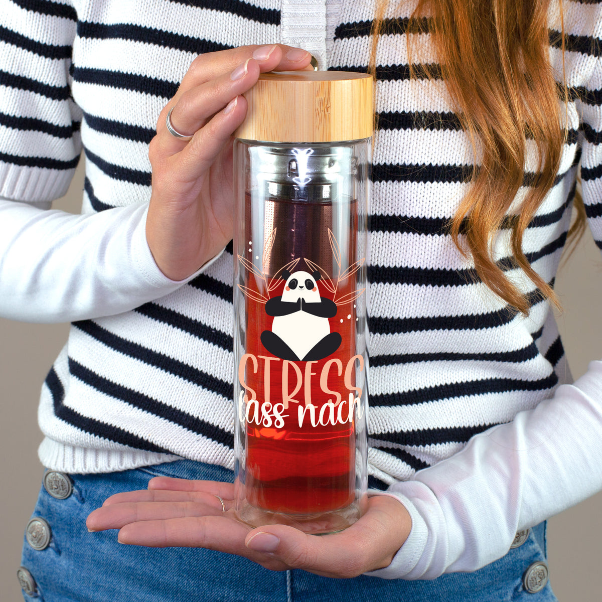 Frau hält doppelwandige Teeflasche aus Glas mit Panda-Aufdruck Stress lass nach, Edelstahl-Sieb und Bambusdeckel