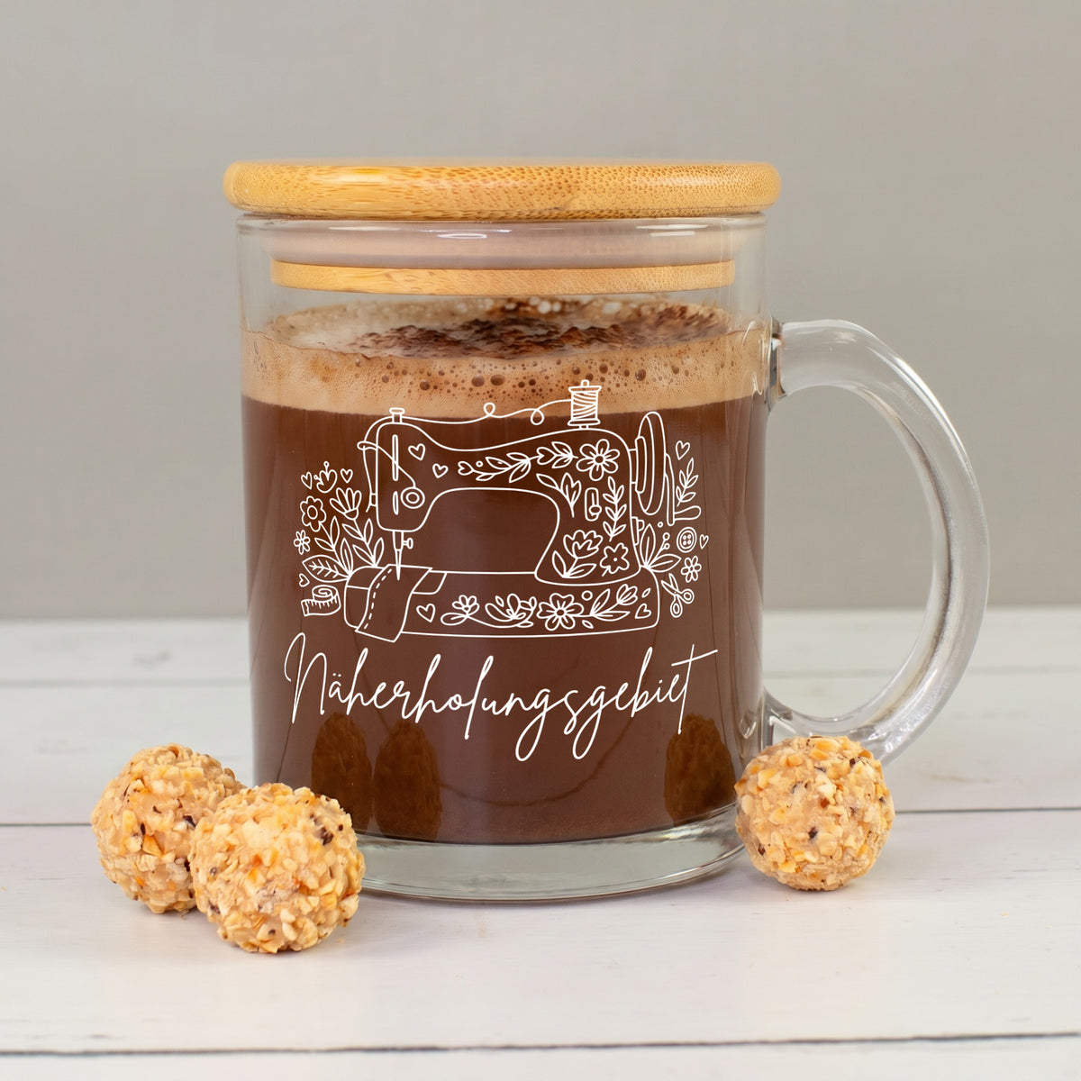 Glastasse mit Kakao, Bambusdeckel und weißem „Näherholungsgebiet“ Nähmotiv neben kleinen Pralinen