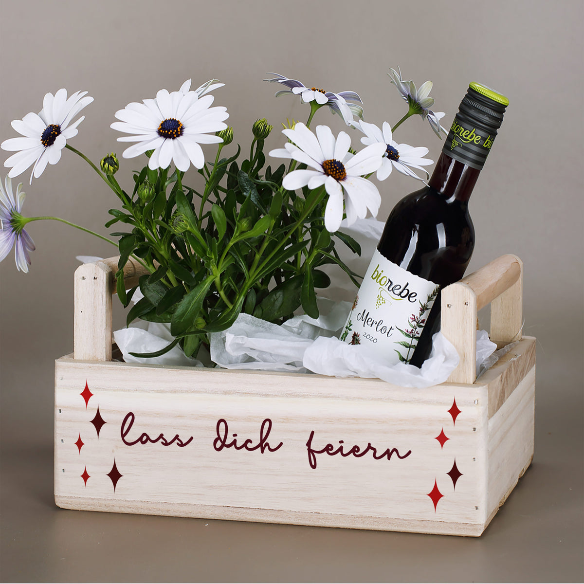 Geschenkkorb aus Holz mit weißen Blumen, Weinflasche und Schriftzug „Lass dich feiern“ als Geburtstagsgeschenk