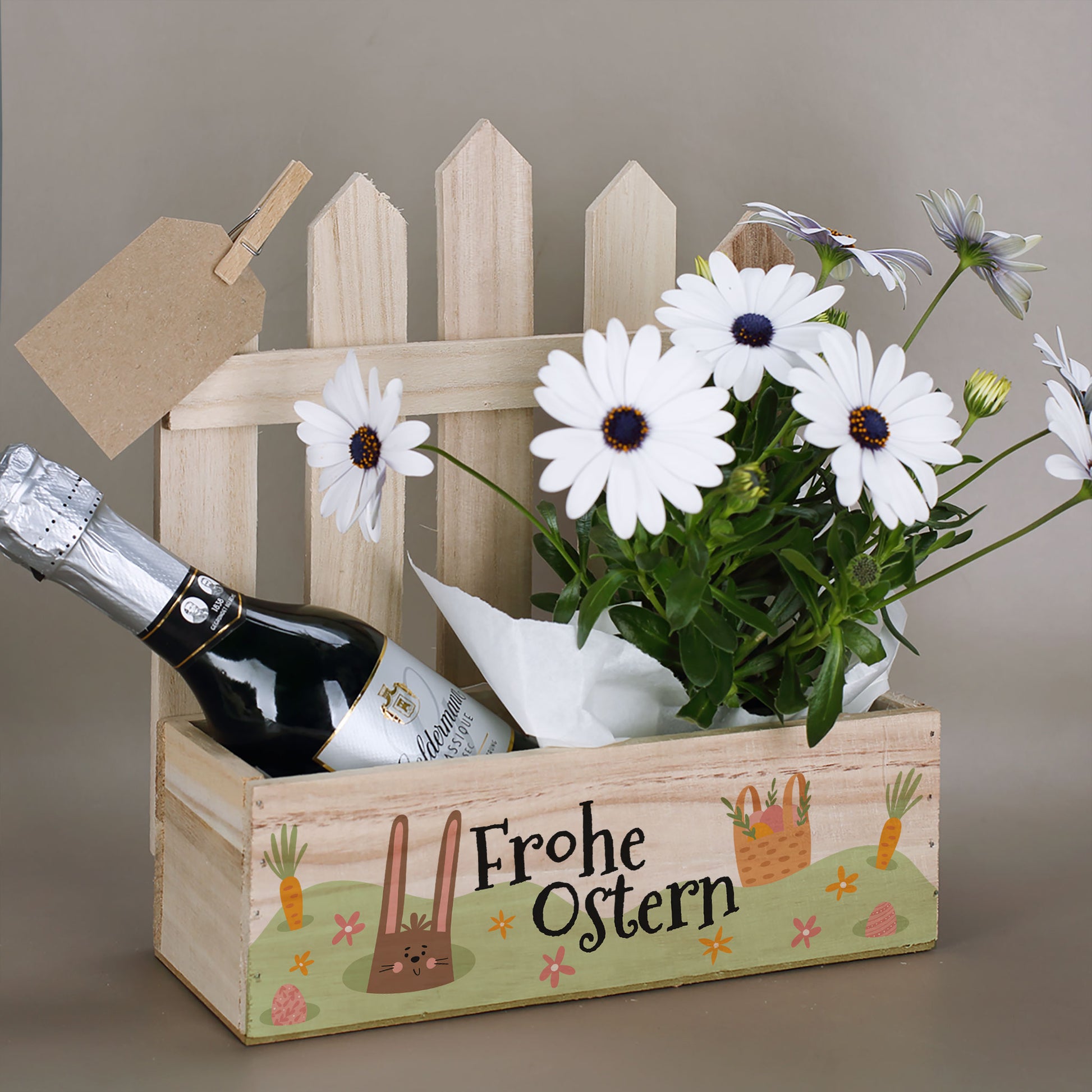 Geschenkkorb aus Holz mit Griff und Osterdesign „Frohe Ostern“, befüllt mit Blumen und Sektflasche
