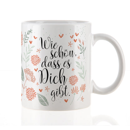 Nahaufnahme der weißen Tasse mit Blumenmuster und Spruch „Wie schön, dass es Dich gibt“ auf weißem Hintergrund.