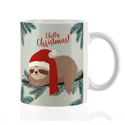 Freigestellte Keramiktasse mit Faultier in Weihnachtsmütze und Schal auf Tannenzweig, Text „Chilly Christmas!“ – neutrale Studioaufnahme.
