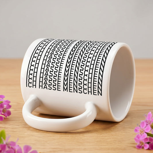 Weiße Keramiktasse mit versteckter Botschaft „Ich hasse Menschen“ liegt seitlich auf einem Holztisch