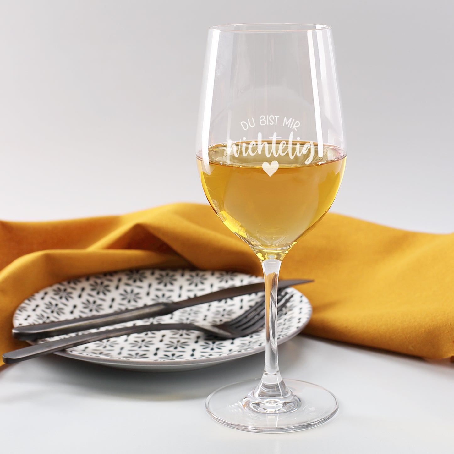 Leonardo-Weinglas aus robustem Teqton-Material, Gravur „Du bist mir wichtelig“, gefüllt mit Weißwein auf gedecktem Tisch.