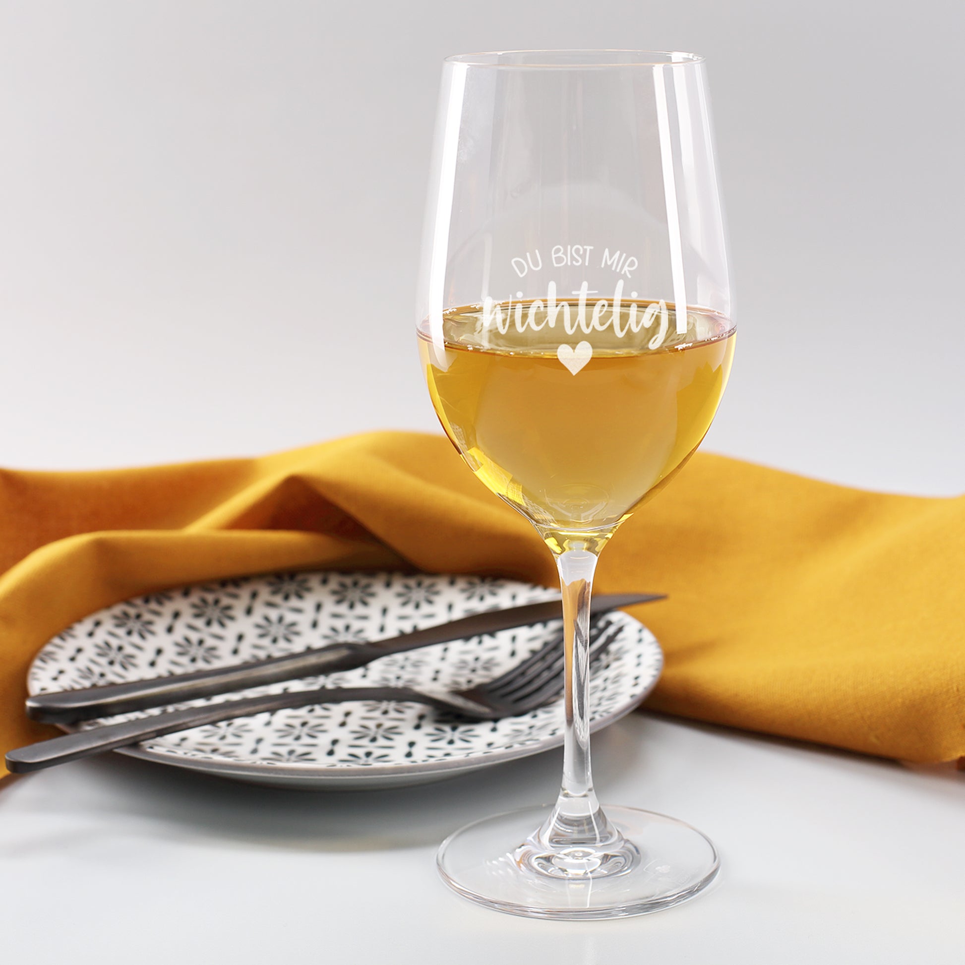 Leonardo-Weinglas aus robustem Teqton-Material, Gravur „Du bist mir wichtelig“, gefüllt mit Weißwein auf gedecktem Tisch.