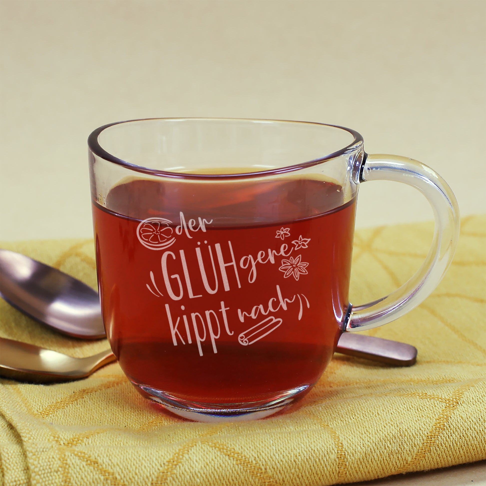 Glasbecher mit Gravur „Der GLÜHgere kippt nach“ von Leonardo, dekoriert mit gelber Stoffserviette und Besteck