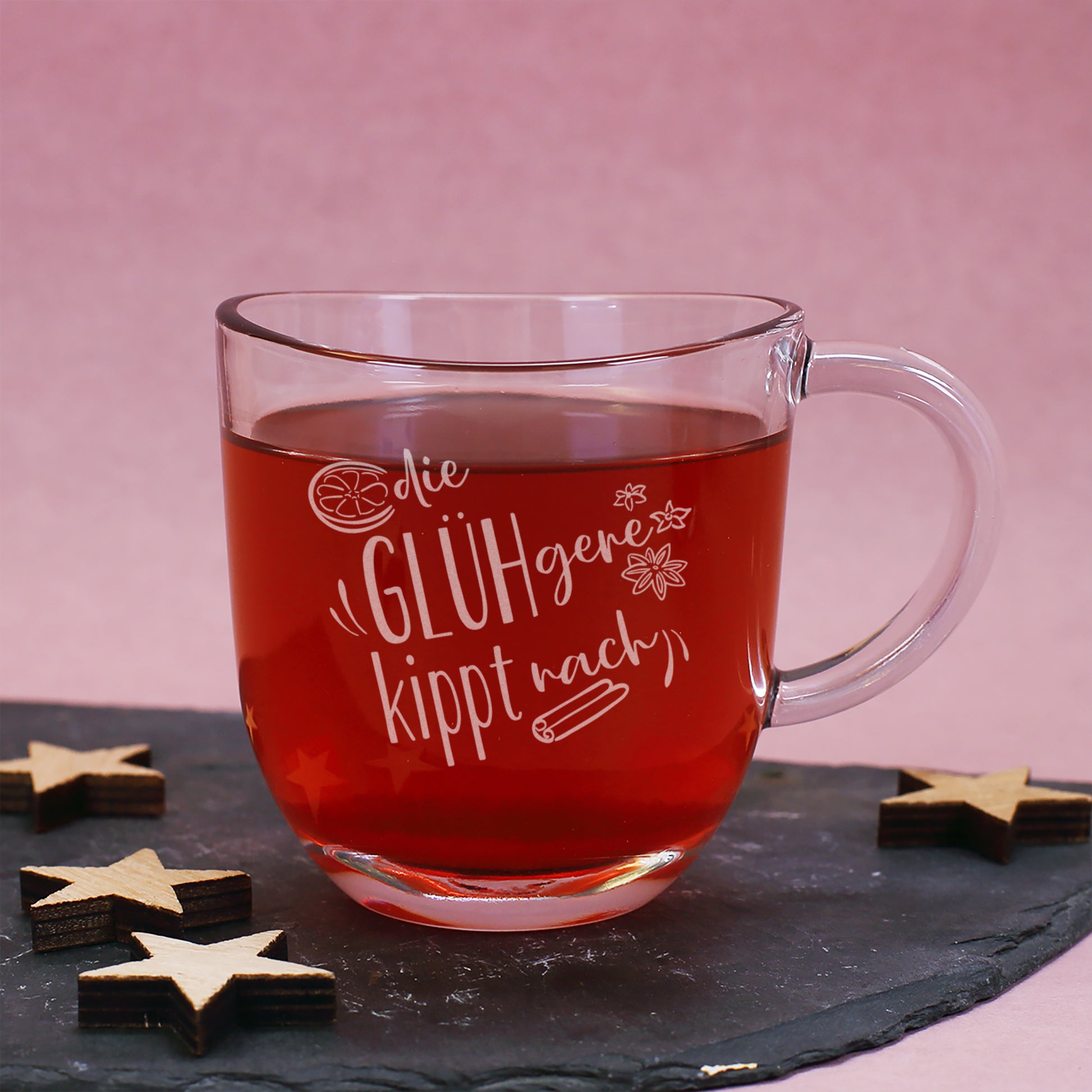 Glasbecher von Leonardo mit Gravur „Die GLÜHgere kippt nach“, auf Schieferplatte mit Holzsternen und Glühweinfüllung