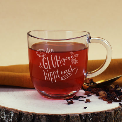 Leonardo Glühweintasse „Die GLÜHgere kippt nach“, befüllt mit Glühwein, auf Holzscheibe mit goldfarbenem Löffel und Teezutaten dekoriert