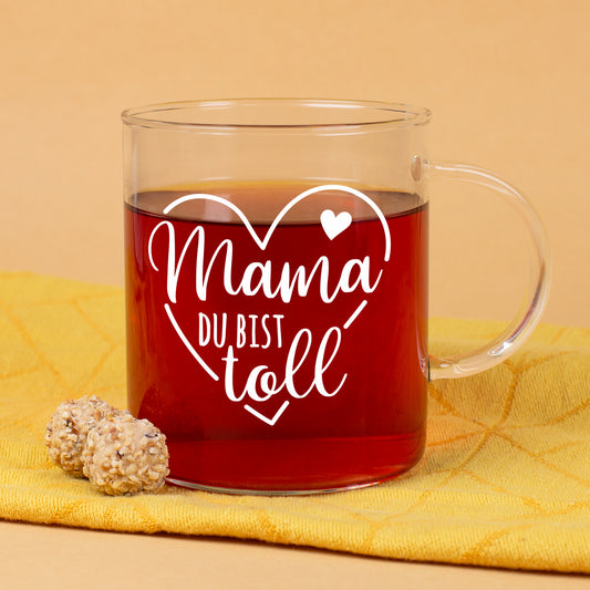 Teeglas mit Aufdruck Mama du bist toll und Herzmotiv auf gelbem Hintergrund mit Gebäck