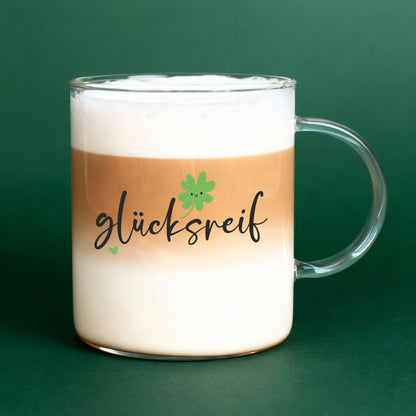 Leonardo-Teeglas „glücksreif“ gefüllt mit Latte Macchiato vor grüner Hintergrundkulisse