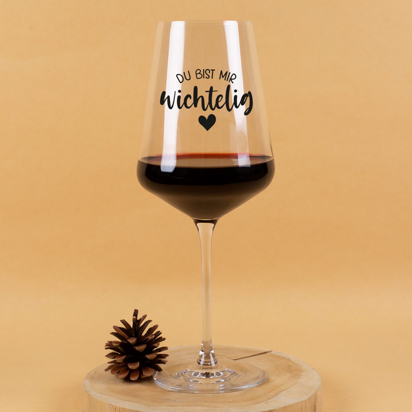 Leonardo Weinglas mit schwarzem Aufdruck „Du bist mir wichtelig“ und Herzmotiv, gefüllt mit Rotwein, dekoriert mit Tannenzapfen