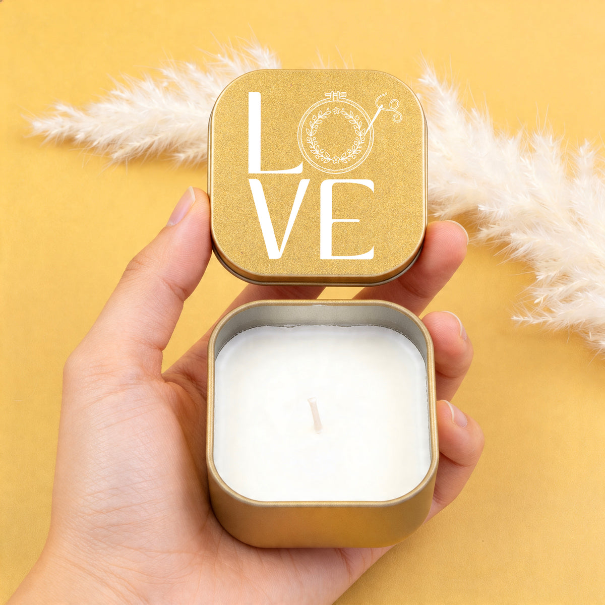 Goldene Mini Duftkerze mit LOVE Schriftzug und floralem Stickrahmen in den Händen