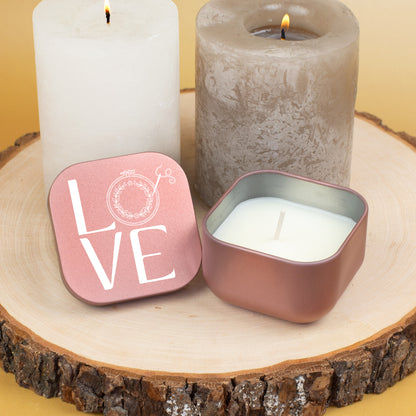 Roségoldene Duftkerze mit LOVE Stickmotiv und geöffnetem Deckel auf Holzdeko