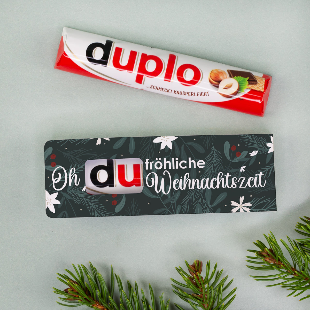 duplo Schokoriegel mit Motiv „Oh du fröhliche Weihnachtszeit“ neben Tannenzweigen