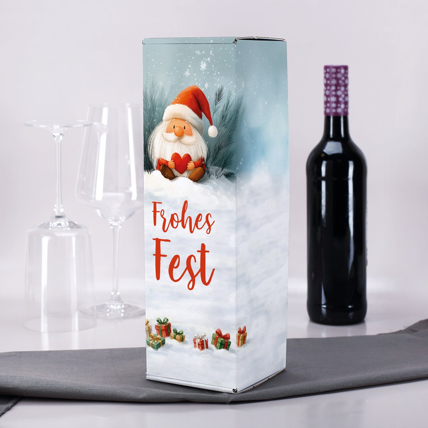 Flaschenkarton mit Wichtelmotiv zwischen Weingläsern und Weinflasche auf hellgrauer Tischdecke