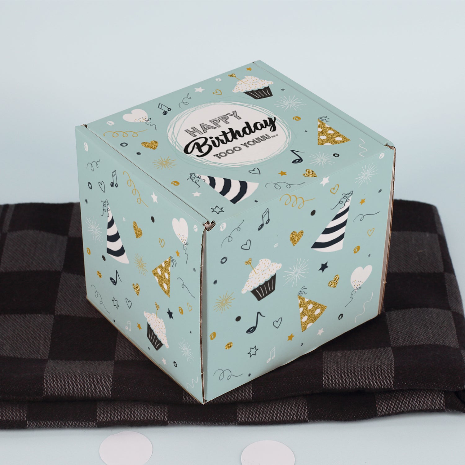 Geschlossene Geschenkbox mit Spruch „Happy Birthday tooo youuu…“ auf kariertem Stoff