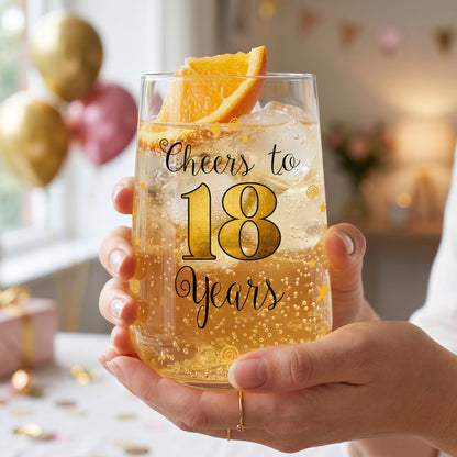 Trinkglas zum 18. Geburtstag mit Cheers to 18 Years Aufdruck und goldenem Design wird in den Händen gehalten