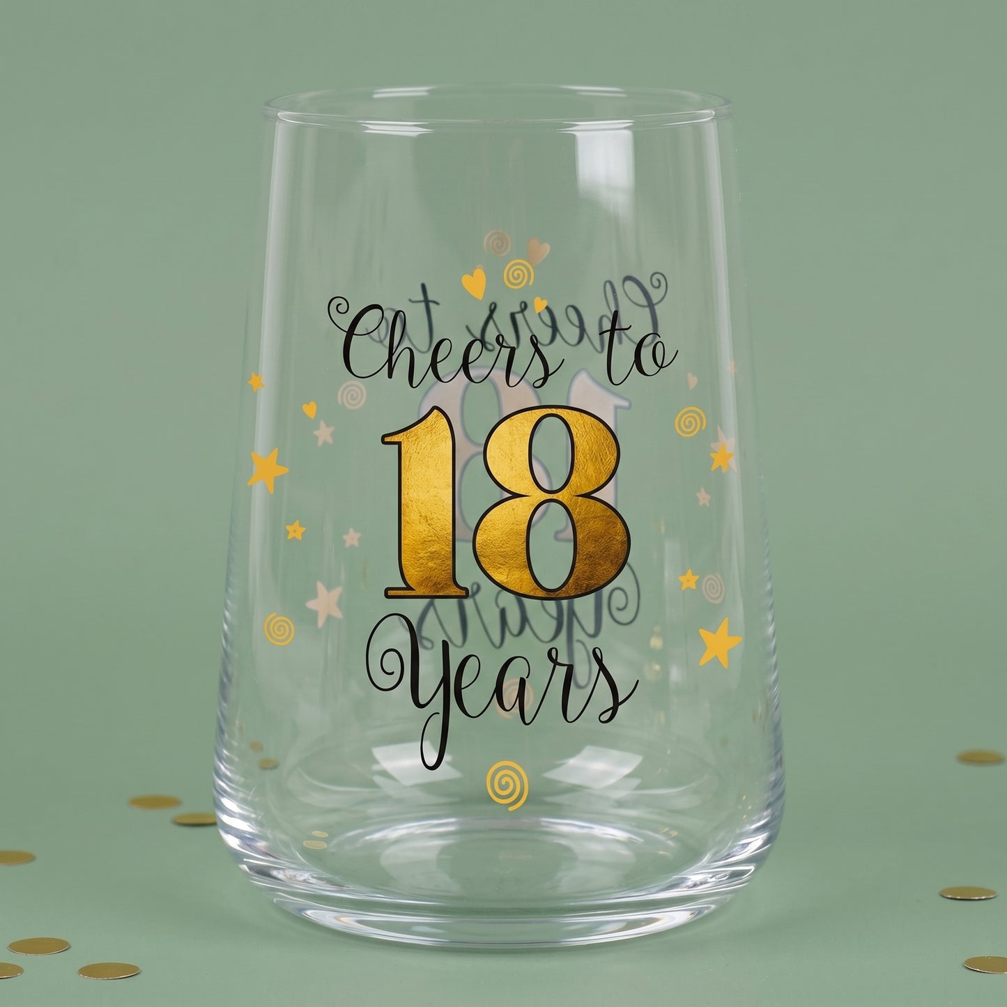 Leeres Trinkglas zum 18. Geburtstag mit goldener 18, Sternen und Konfetti auf grünem Hintergrund