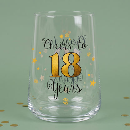 Leeres Trinkglas zum 18. Geburtstag mit goldener 18, Sternen und Konfetti auf grünem Hintergrund