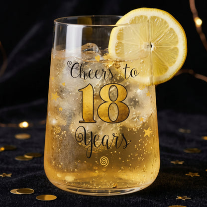 Trinkglas mit Cheers to 18 Years Design, Zitronenscheibe und goldenem Getränk auf dunklem Hintergrund